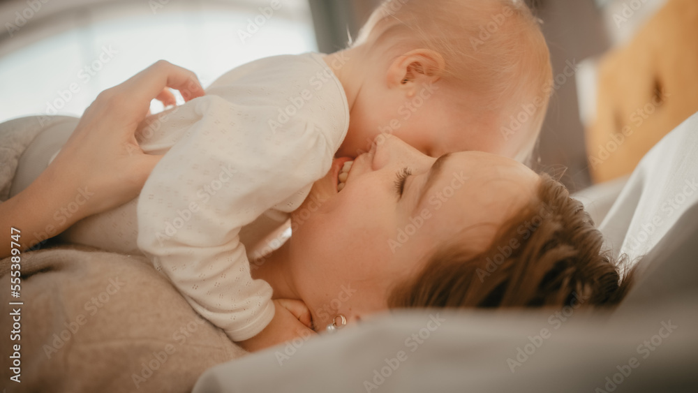 Loving Young Caring Mother Playing and Nursing Adorable Baby at Home. Smiling Beautiful Mom and Cute