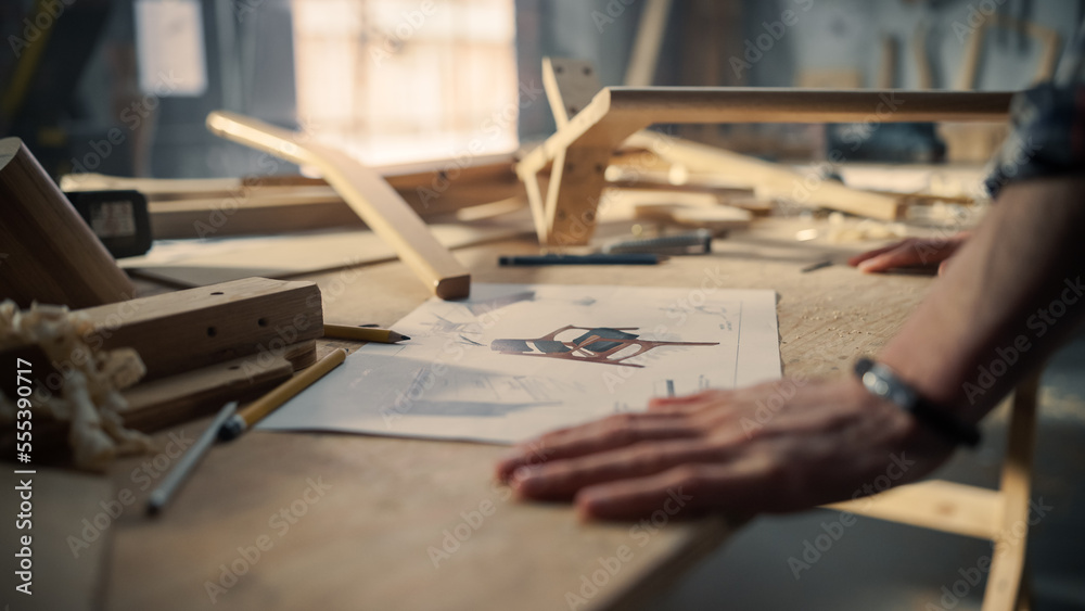 Young Carpenter Reading Blueprints and Starting to Assemble Parts of a Wooden Chair with a Rubber Ha