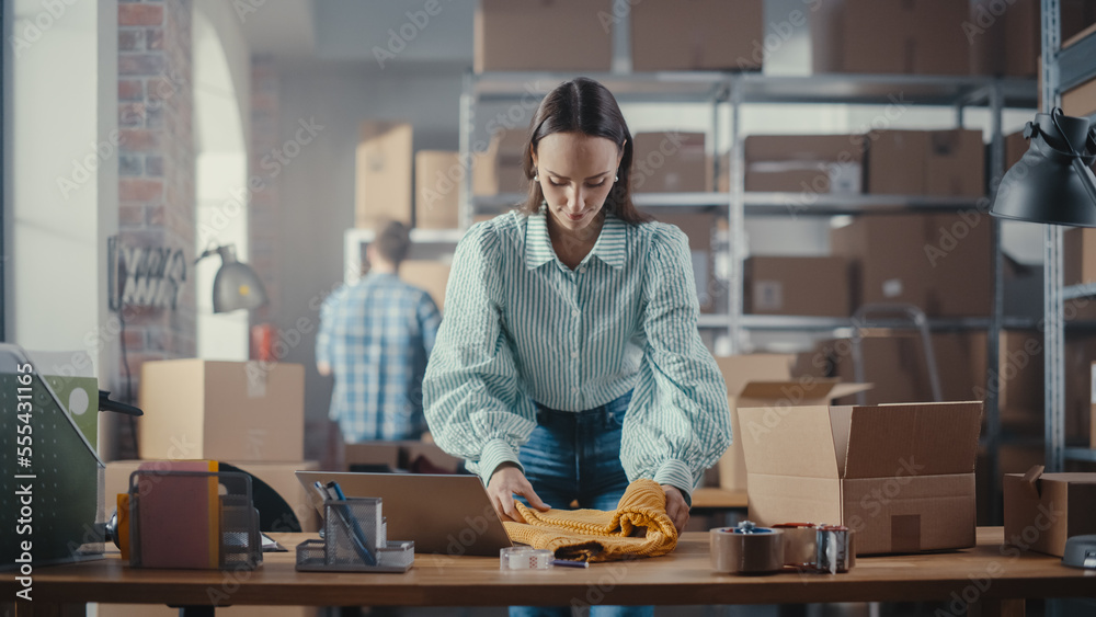 Small Business Owner of an Online Store Works on Laptop Computer while Leaning On Her Desk in Wareho