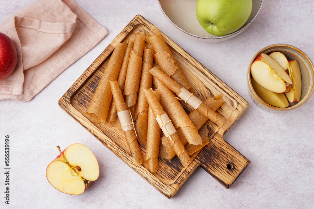 Wooden board with tasty apple pastilles on light background