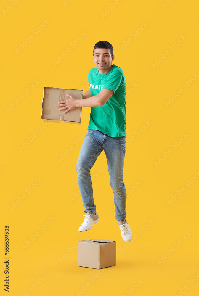 Young volunteer with cardboard boxes jumping on yellow background