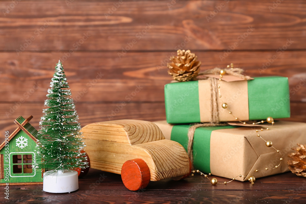 Toy car with Christmas tree, decorations and gift boxes on wooden background