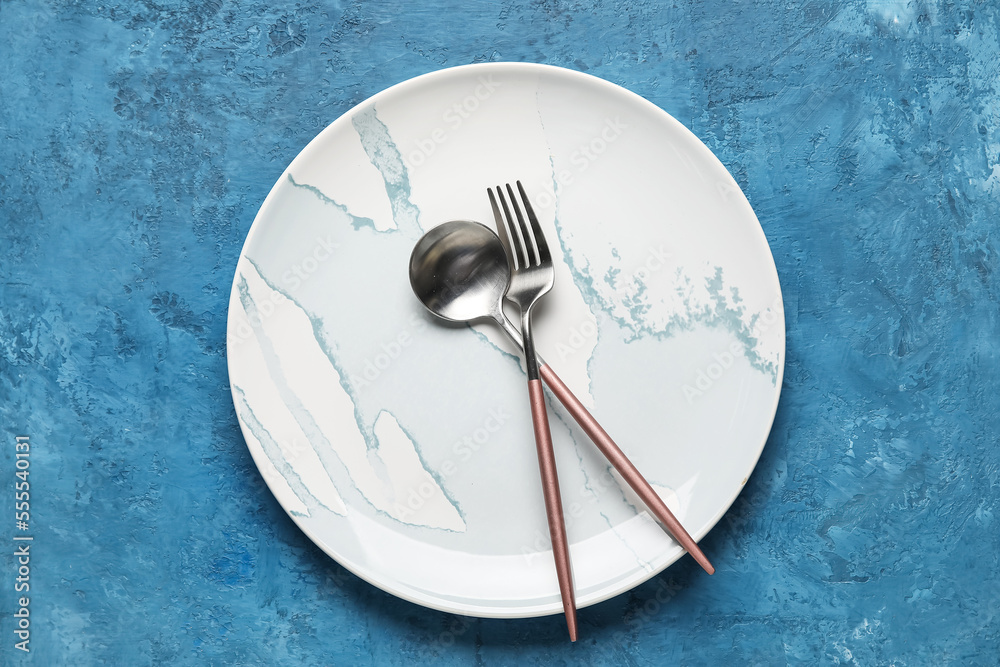 Stylish plate with cutlery on blue background