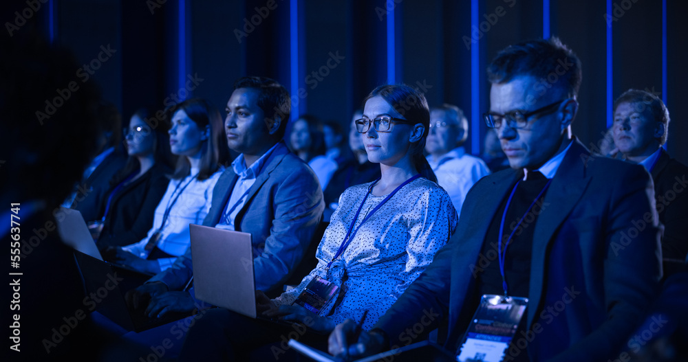 Young Woman Sitting in a Crowded Audience at a Business Conference. Female Delegate Using Laptop Com