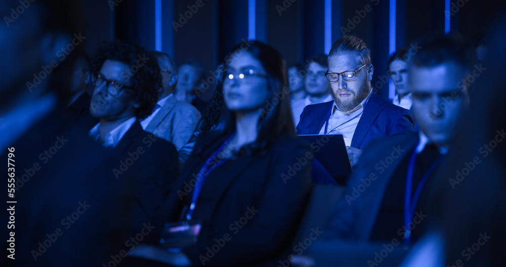 Young Bearded Man Attending an IT Conference in Crowded Audience. Delegate Using Laptop Computer. Ha