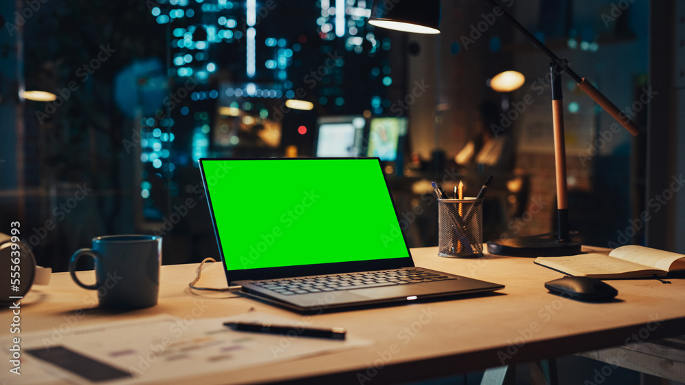 Laptop Computer Display with Mock Up Green Screen on a Table in Agency Office in the Evening. Chroma