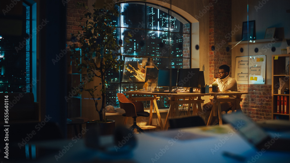 Focused Project Manager Sitting at a Desk, Working Alone on a Computer in an Office at Night. Africa