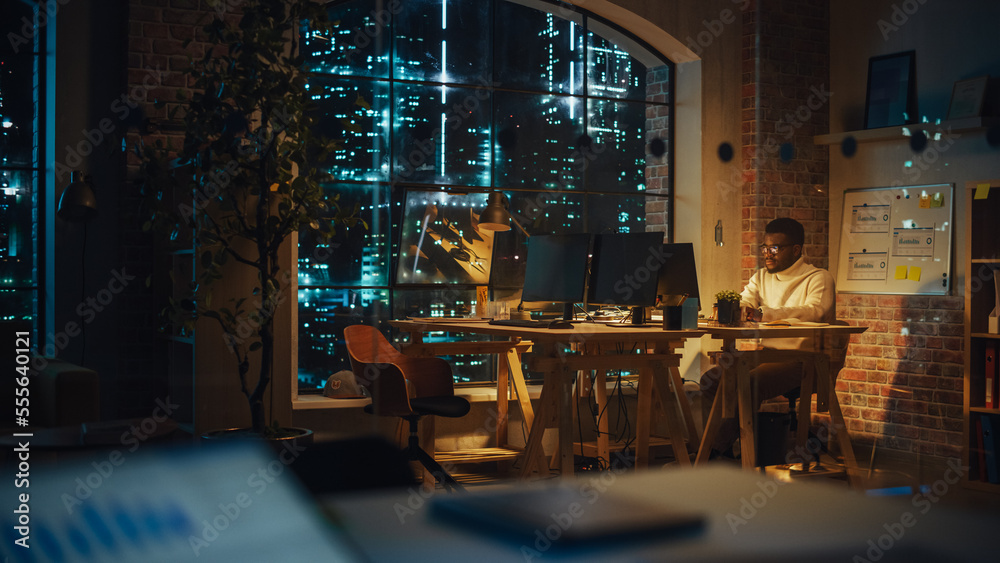 Focused Project Manager Sitting at a Desk, Working Alone on a Computer in an Office at Night. Black 