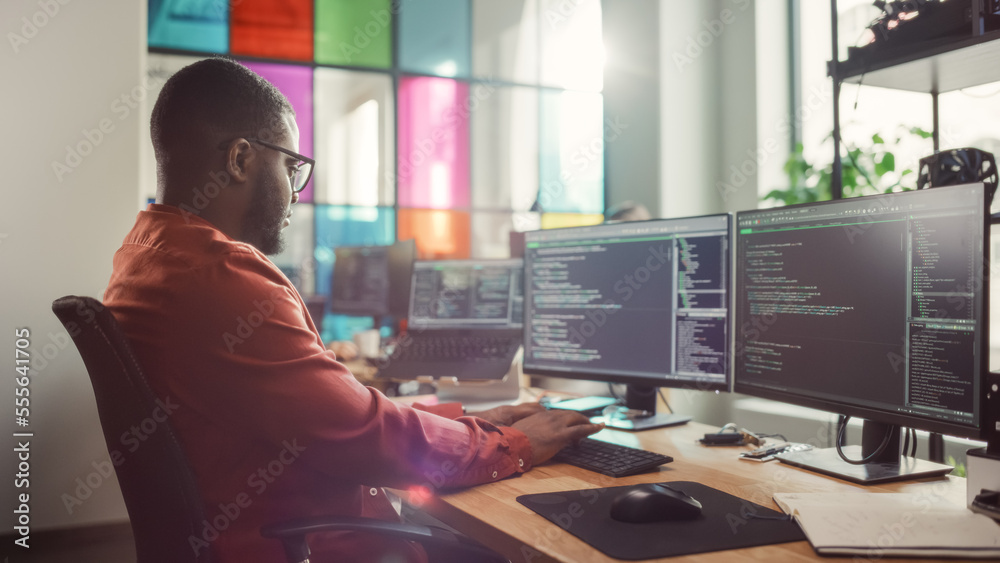 African American Man Coding on Desktop Computer with Professional Multiple Monitors Setup in Creativ