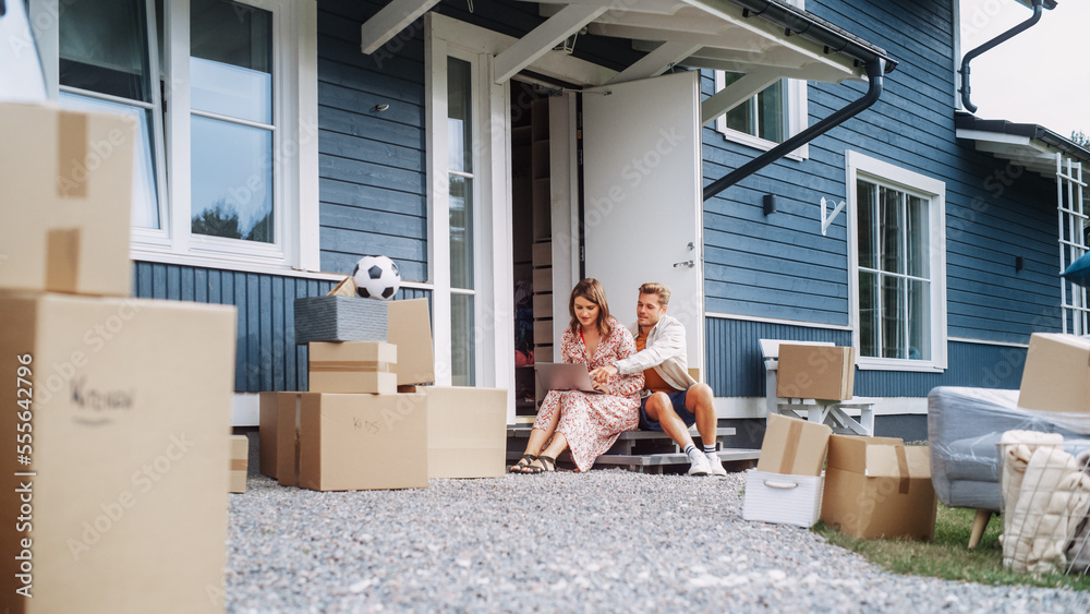 Young Beautiful Couple Sitting on a Front Porch of Their New House, Using Laptop Computer. Female Sh