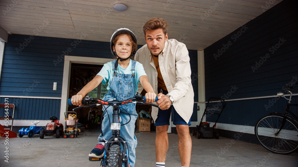 Happy Father Showing His Daughter to Ride a Bicycle on the Lawn in The Front Yard of Their Home. You