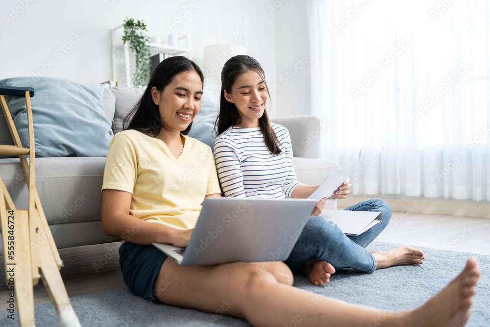 Asian woman amputee using laptop computer with friend in living room. Attractive young legless girl 