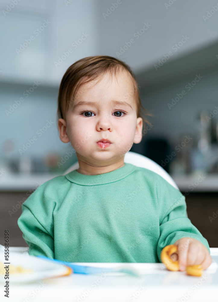 Baby eating food on kitchen. Cute little baby eating healthy food at home.