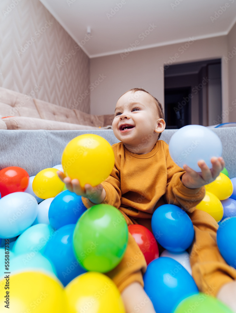 Portrait of a smiling infant sitting among colorful balls. Child playing in ball pit. Activity toys 