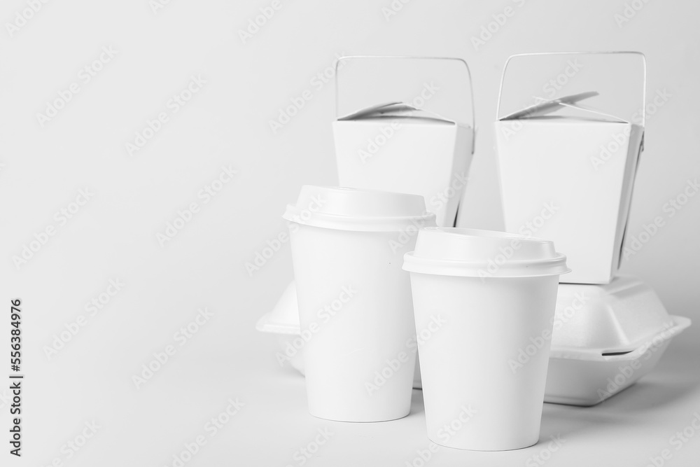 Paper cups and different food containers on light background