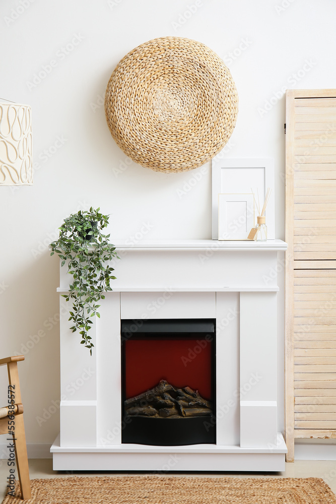 Fireplace with blank photo frames, reed diffuser and houseplant near white wall in room