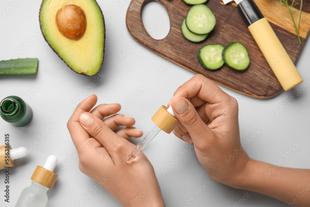 Woman applying essential oil onto hand on light background, closeup