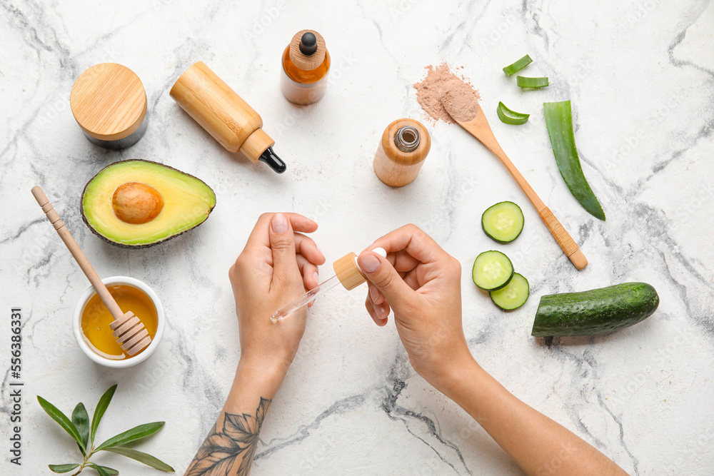 Woman applying essential oil onto hand on light background