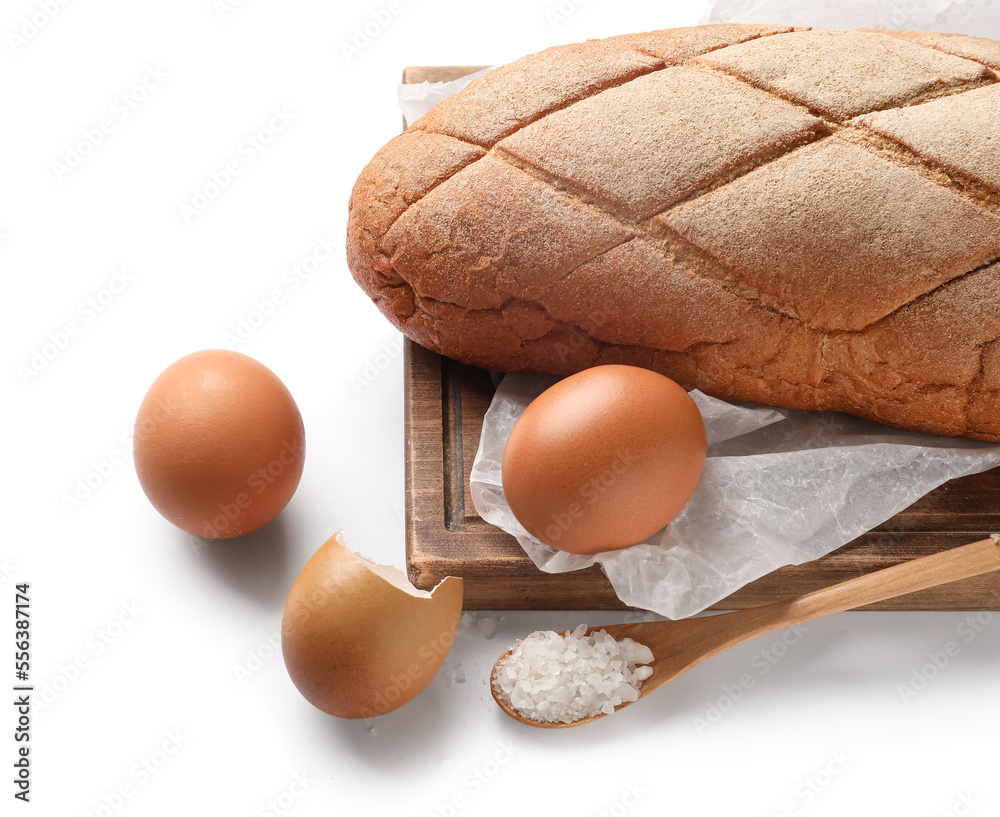 Wooden board with loaf of fresh bread and eggs on white background, closeup