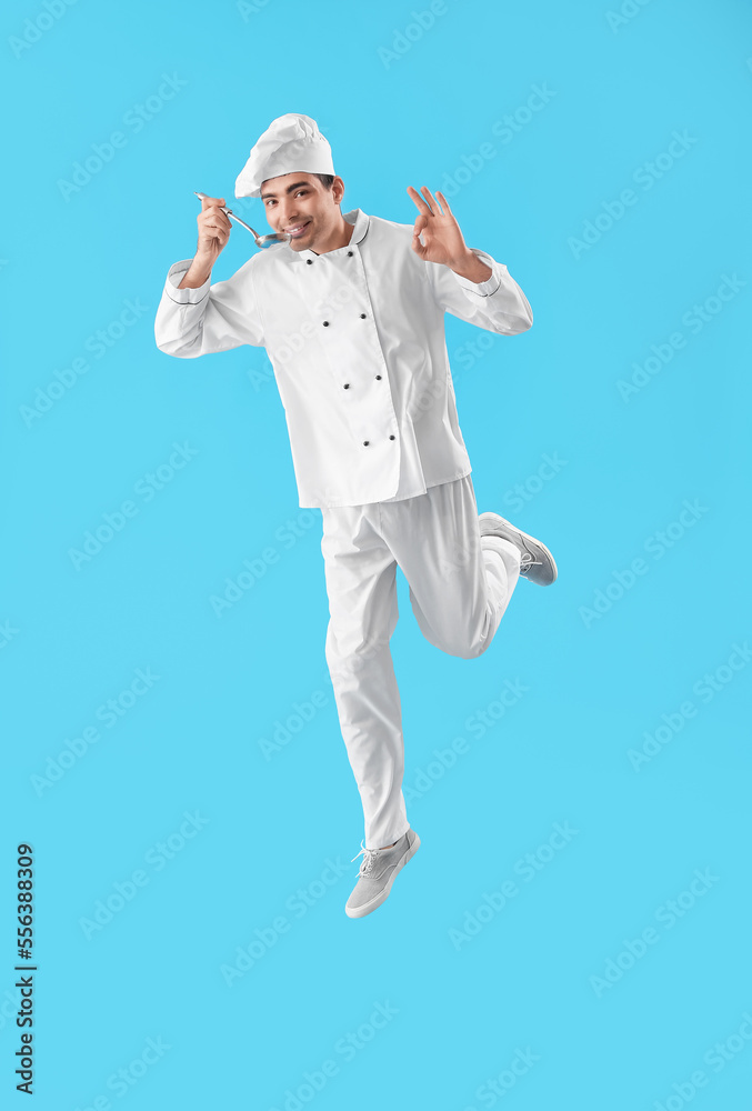 Young chef with ladle showing OK while jumping on blue background