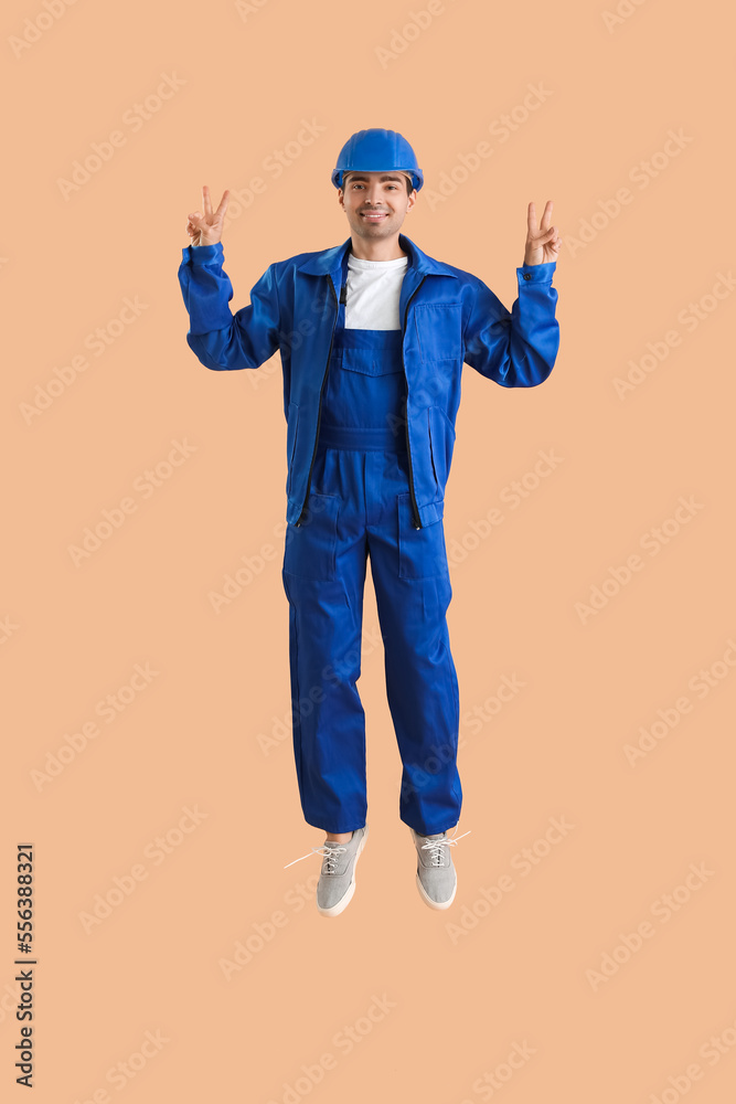 Young male worker showing victory gesture while jumping on beige background