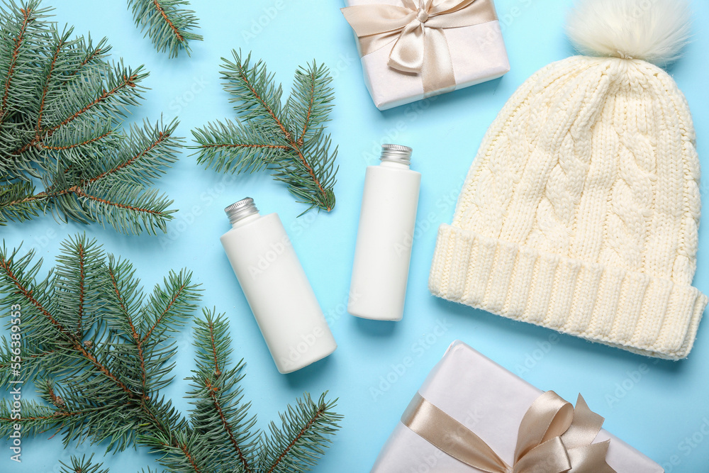 Composition with bottles of cosmetic products, warm hat, Christmas gifts and fir branches on color b