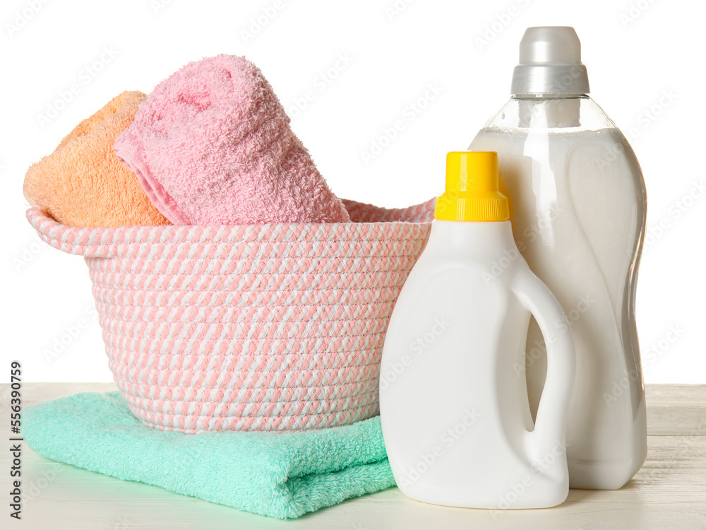 Laundry detergents and basket with towels on table against white background