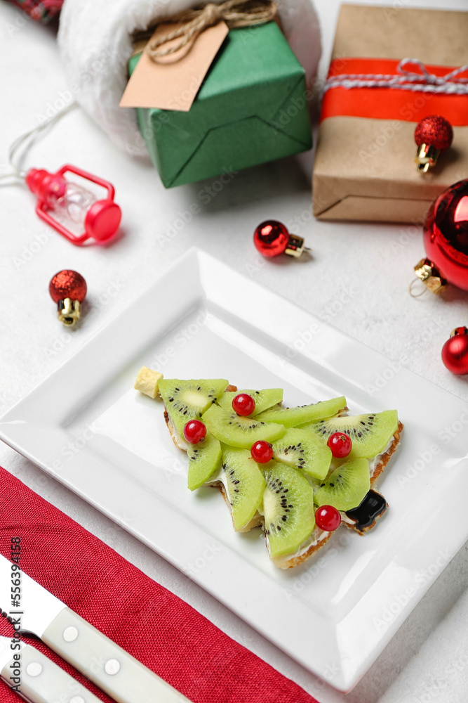 Plate with tasty Christmas tree pancake with fruits and gifts on light background, closeup