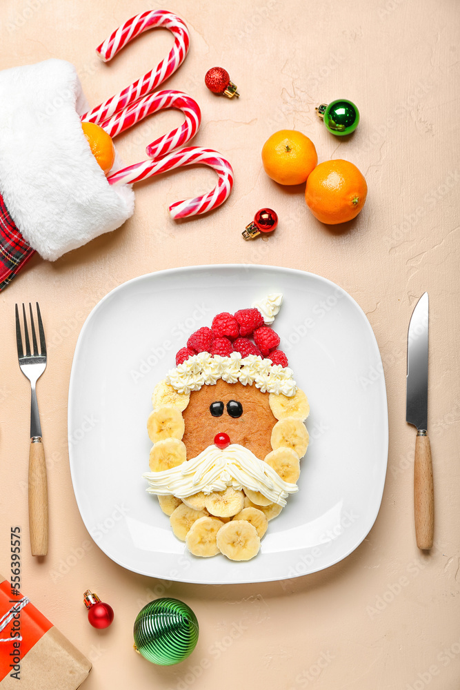 Plate with Santa Claus made of pancake, fruits, whipped cream and Christmas decor on beige table