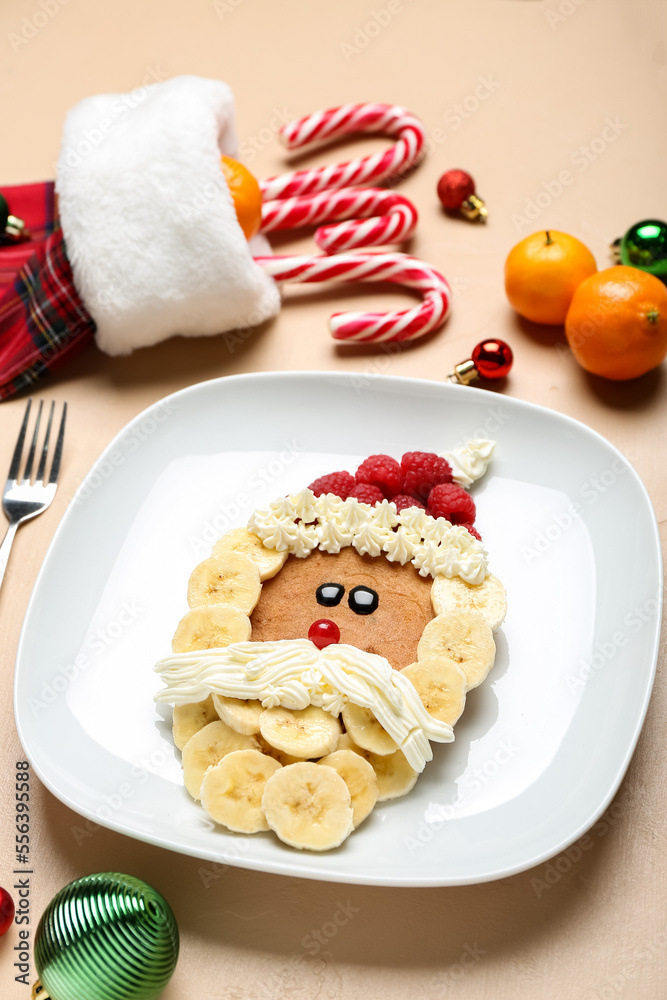 Plate with Santa Claus made of pancake, fruits, whipped cream and Christmas decor on beige table, cl