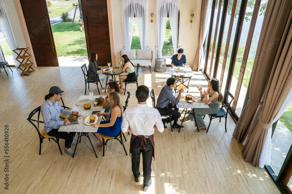 Caucasian waiter serving food to group of diverse customer in restaurant.