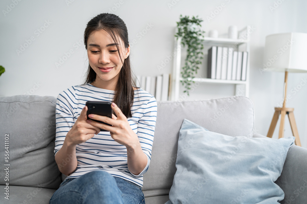 Asian beautiful woman sitting on sofa and swipe mobile phone in house. 