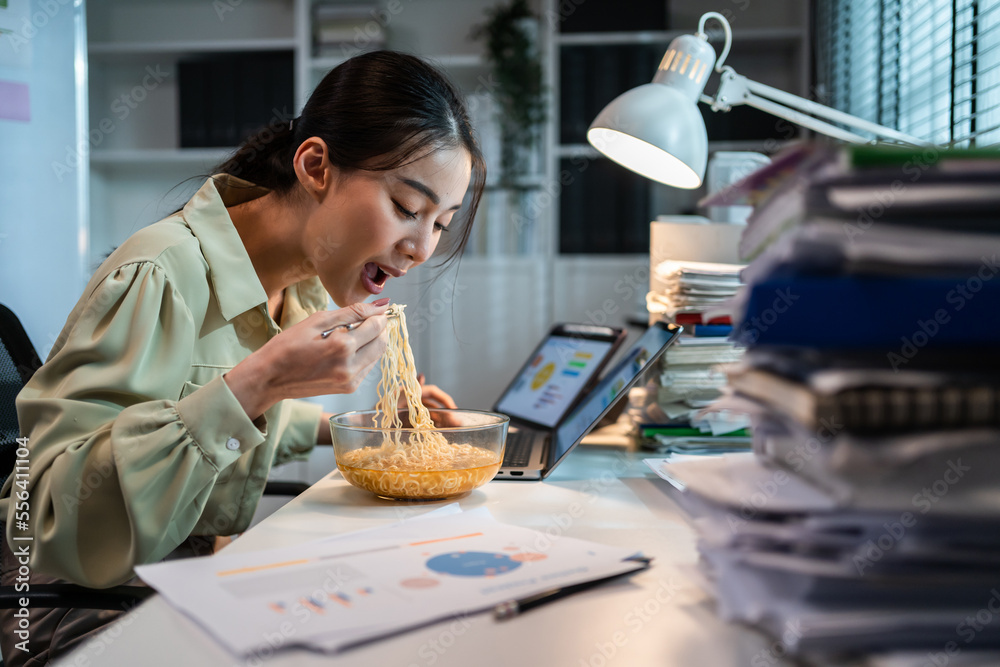 Asian young businesswoman eating noodles while work in office at night.