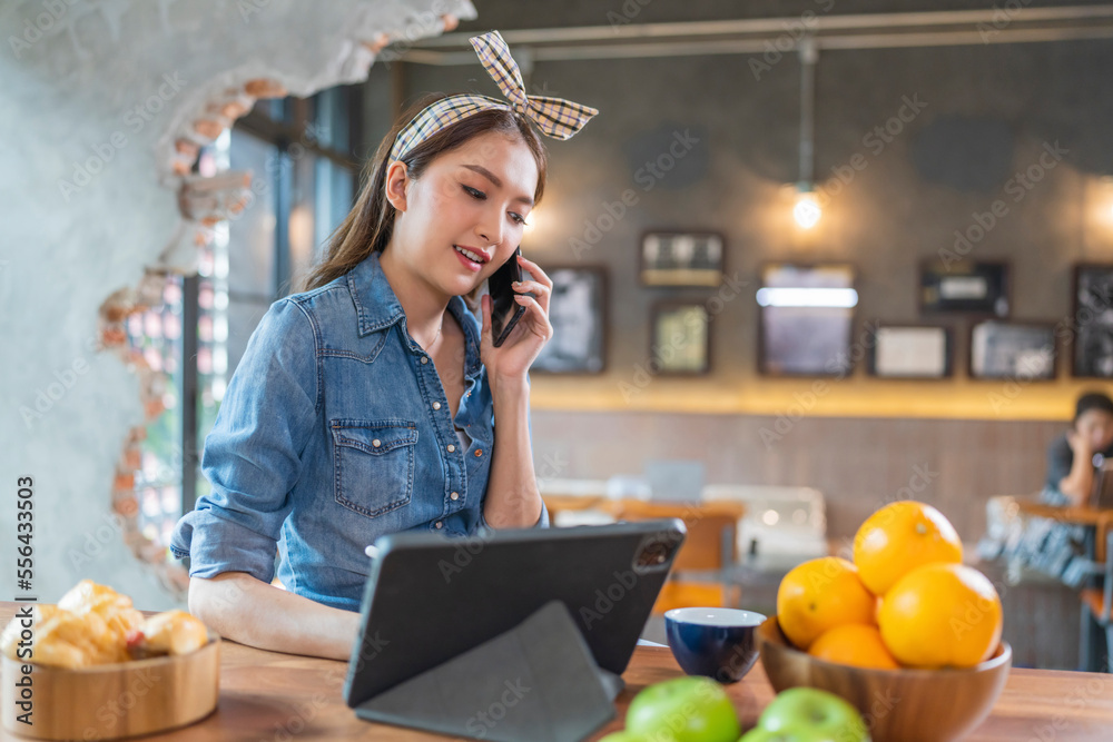 asian female cheerful woman hand using smartphone tablet working from kitchen at home while drink co