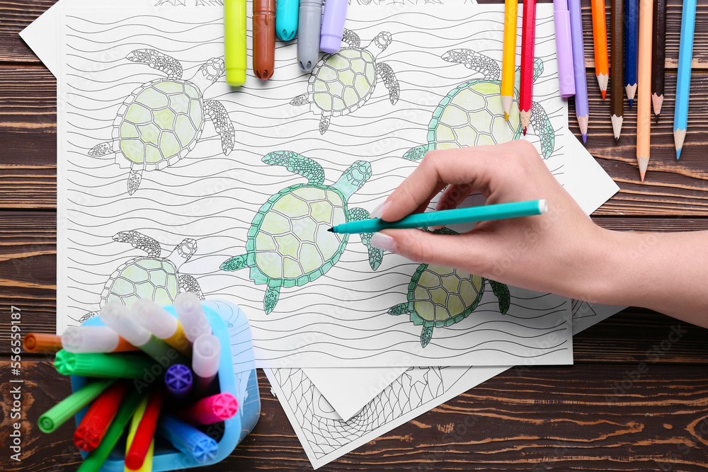 Woman coloring page with felt-tip pen on dark wooden background