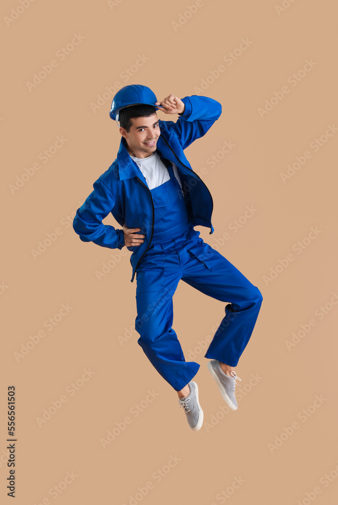 Young male worker jumping on beige background