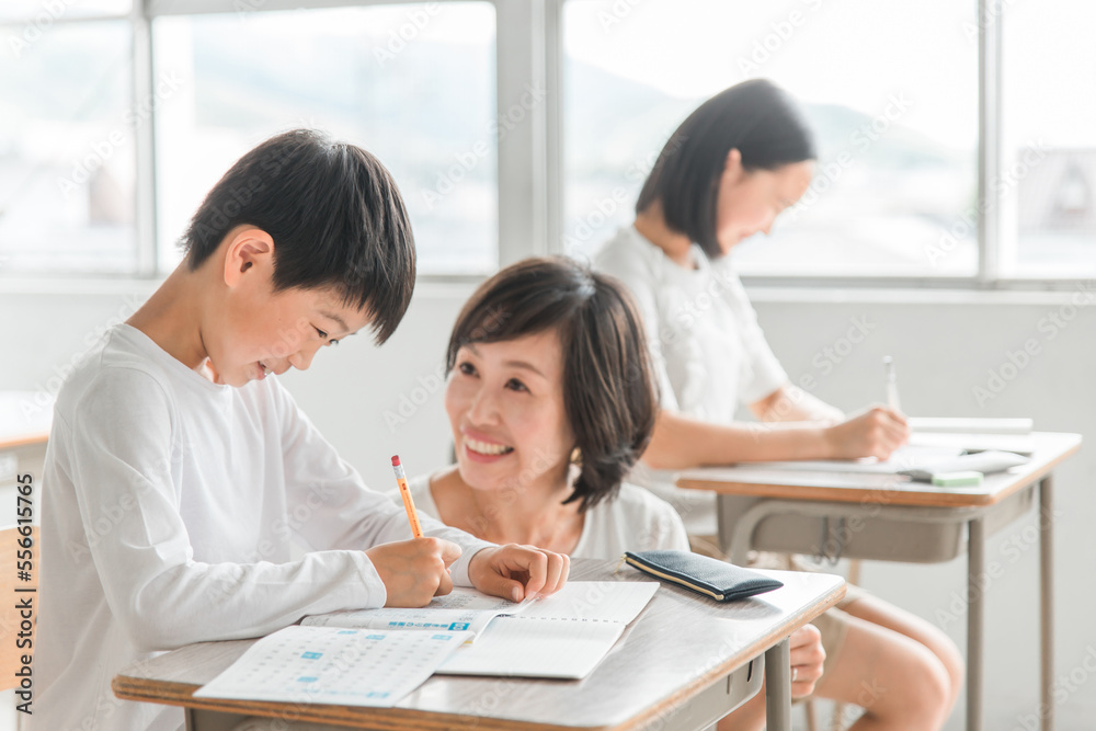 学校の教室・塾で先生と話す高学年のアジア人男子生徒（学習・教育） 