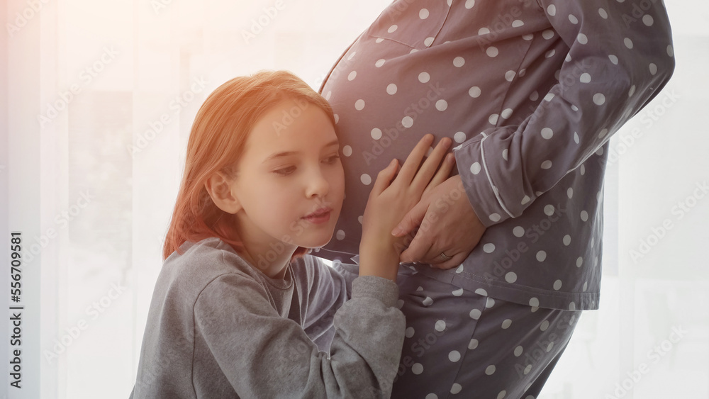 初中生在家里用白色窗帘抚摸怀孕母亲的肚子。棕色头发的女孩哇