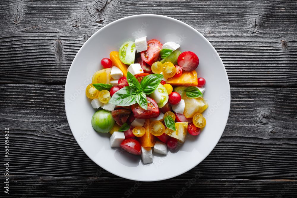 Salad with different varieties kind of red, yellow, green and black tomato mix, mozzarella cheese an