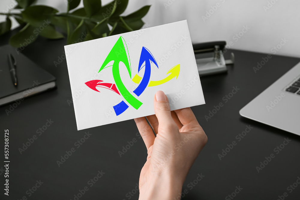 Woman holding paper sheet with drawn arrows at office table, closeup. Concept of choice