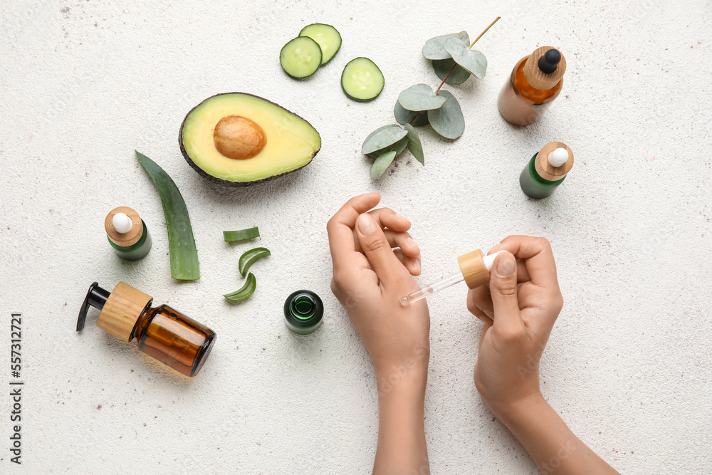 Female hands with bottles of essential oil and natural ingredients on light background