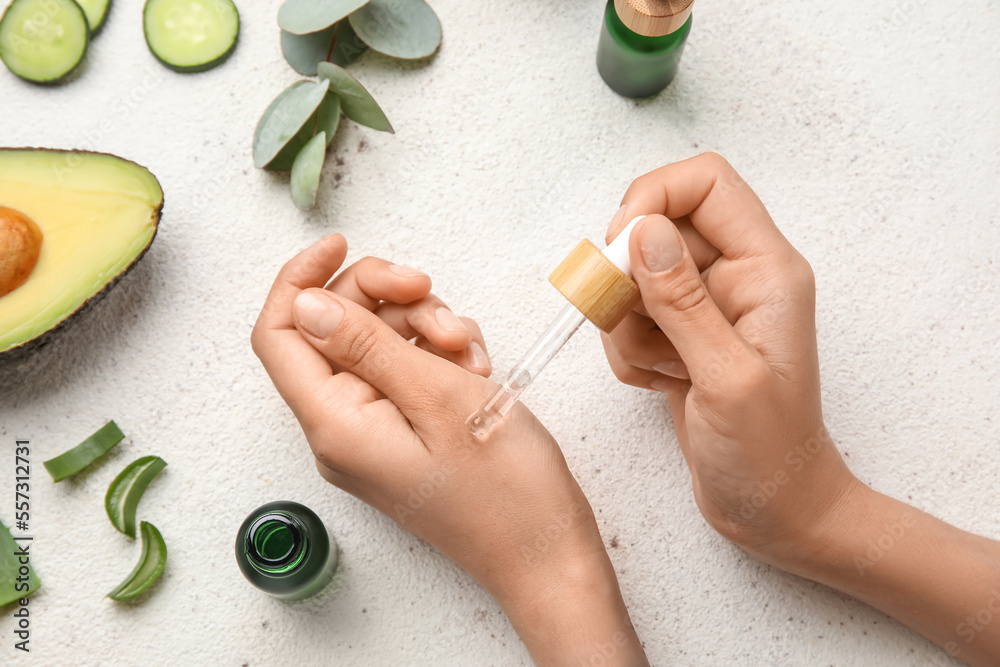 Woman applying essential oil on light background