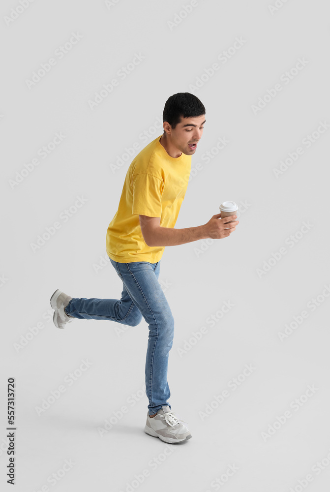 Young man with cup of coffee jumping on light background