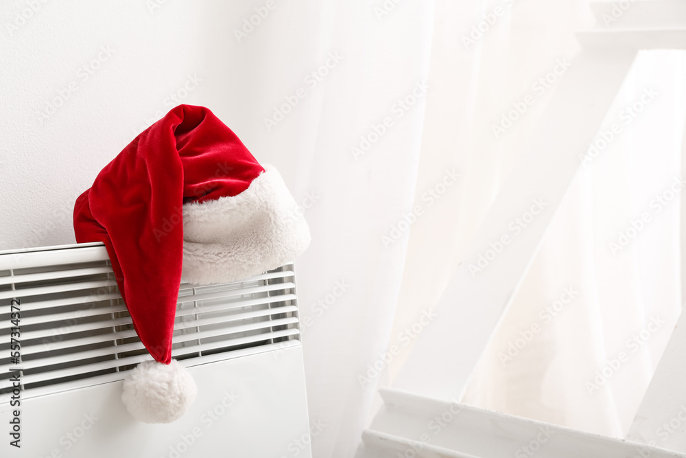 Santa hat on electric radiator near light wall, closeup