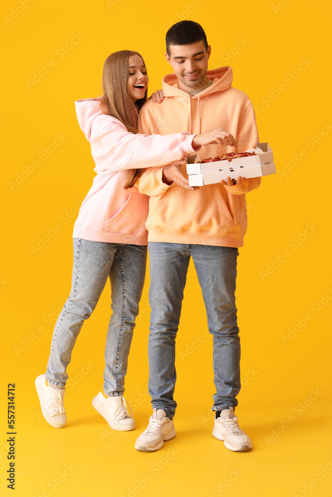 Happy young couple with fresh pizza on yellow background