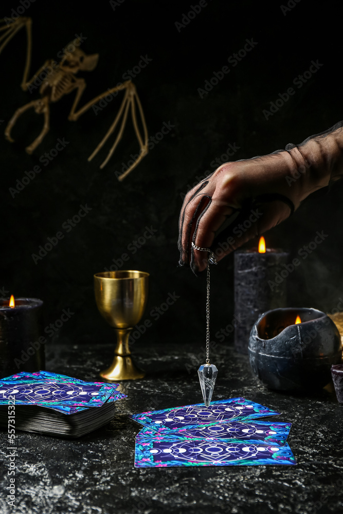 Fortune teller using pendulum and tarot cards to read future on dark background