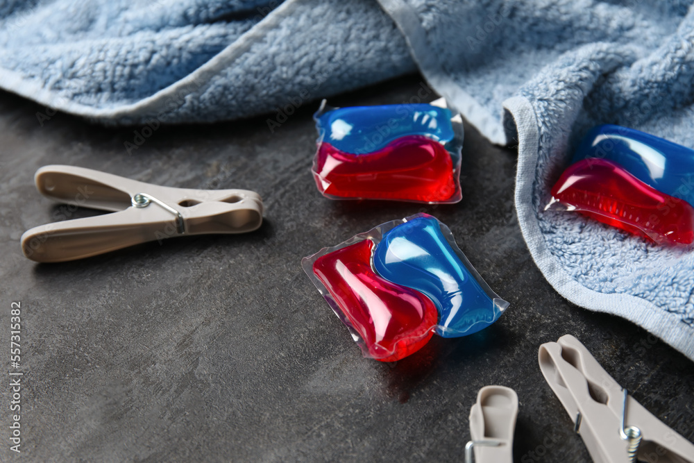 Capsules with laundry detergent, clothespins and towel on black background