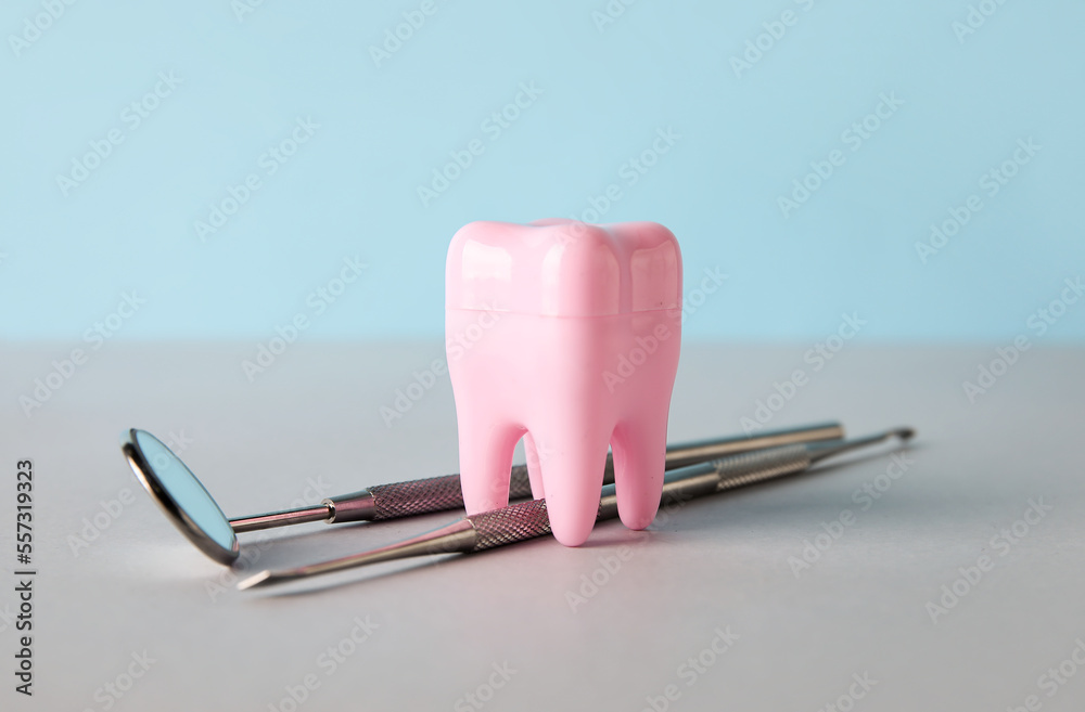 Plastic tooth with dental tools on table against blue background