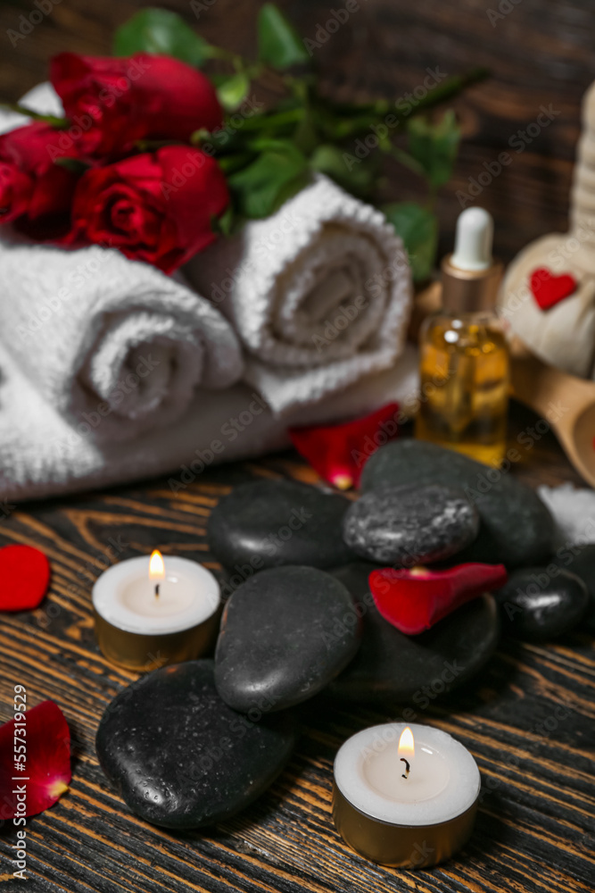 Spa stones with candles and rose petals on dark wooden table, closeup. Valentines Day celebration