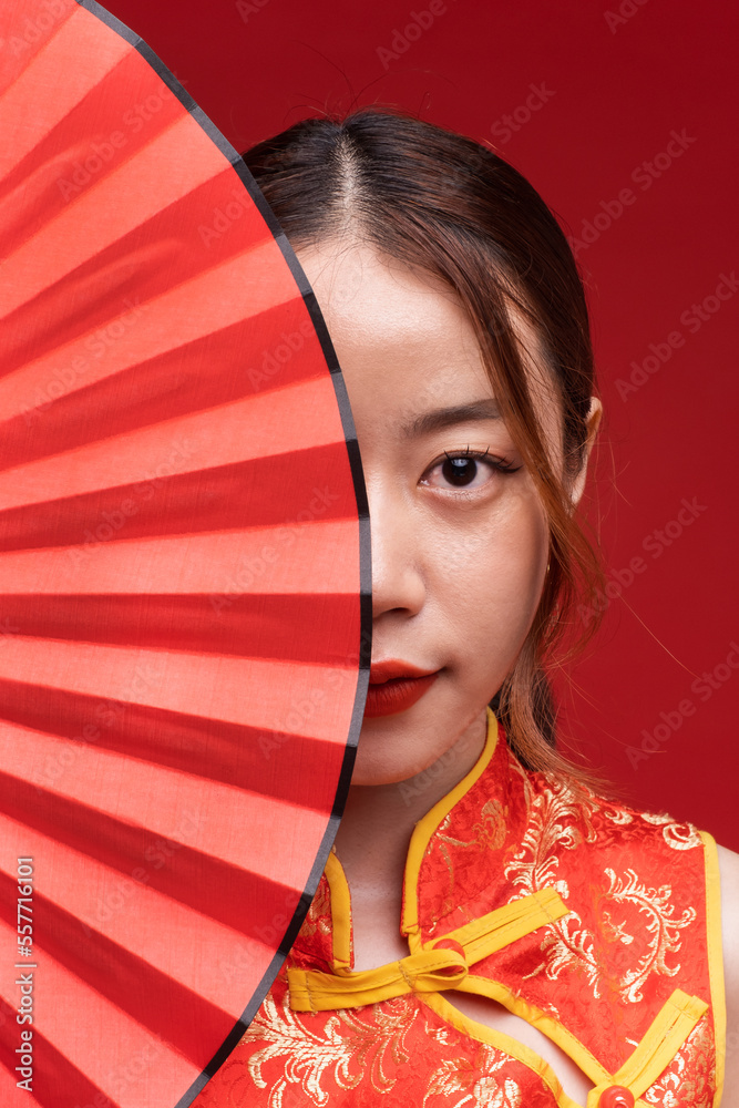 Young asian woman wearing qipao cheongsam dress with Chinese folding fan on red background for Chine